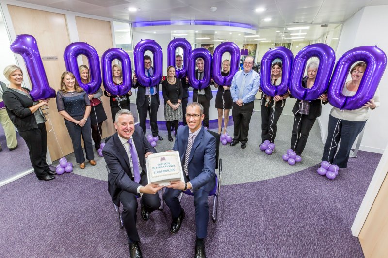 People holding up the number one billion on balloons