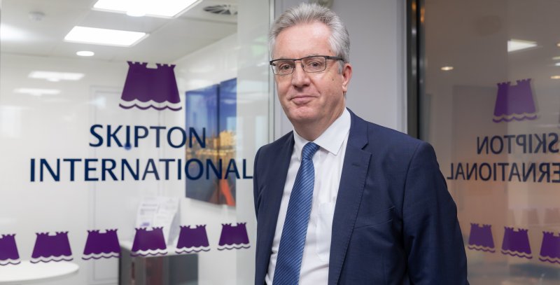 man smiling next to Skipton logo