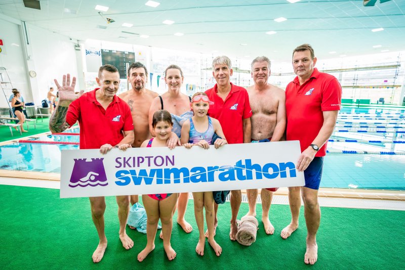 people smiling in front of Skipton Swimarathon logo