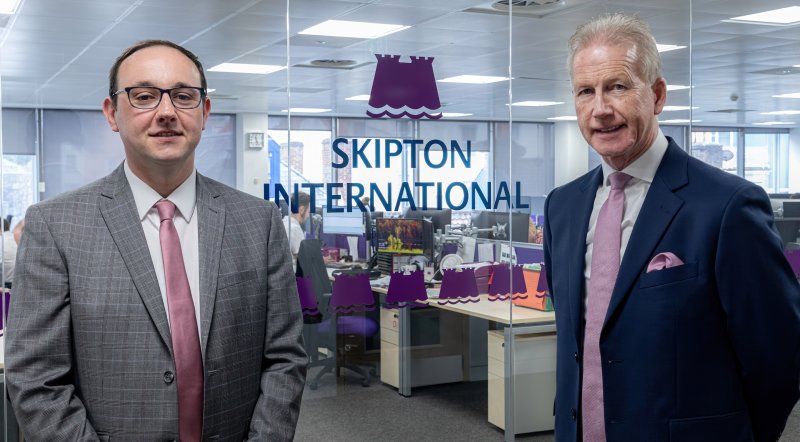 people smiling in front of Skipton logo